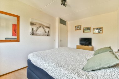 Rahat bir yatak odası, dekoratif yastıklar ve duvar resimleri. Mekan aydınlık ve minimalist, rahatlamak ve rahatlamak için ideal..