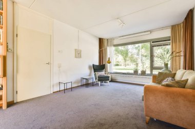 Rahat bir oturma odası, doğal ışıklandırması olan büyük pencereler ve sıcak bir atmosfer yaratan şık dekoratif unsurlar..