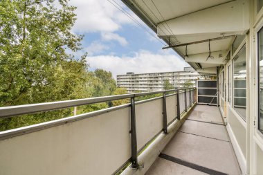 Geniş, modern bir apartman balkonunda tırabzan, yeşillik ve şehir mimarisi, rahatlama ve açık hava keyfi için ideal..