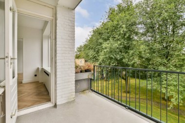 Açık bir kapı ve canlı bir yeşillik içeren sakin bir balkon manzarası. Uzay, doğal ışık ve manzaralı sakin bir atmosfer sunuyor..
