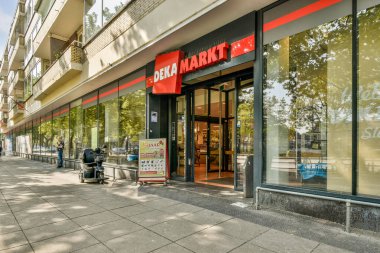Modern bir süpermarkette büyük cam pencereler, canlı bir tabela ve kentsel bir ortamda davetkar bir giriş, modern mimari ve müşteri erişimi sergilenmektedir..