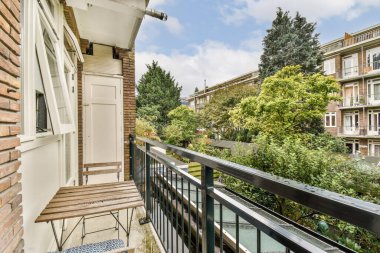 Tuhaf bir balkon, dingin bir ortamda rahatlamak için ideal yeşil ve kentsel mimariye tepeden bakan ahşap bir bank içerir..