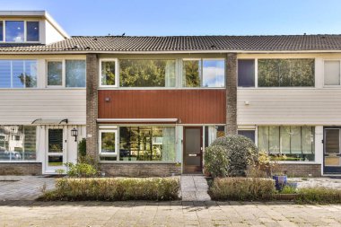 Önünde büyük pencereler ve yeşillikler bulunan, simetrik bir cephe ve davetkar bir atmosfer gösteren çağdaş bir konut yapısı..