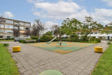Çimenli alanlar, ağaçlar ve slaytlı bir oyun alanı olan huzurlu bir şehir parkı. Tasarım, aileler için rahatlama ve dinlenme etkinlikleri çağrısında bulunuyor.