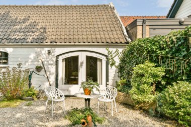 Beyaz sandalyeler ve yemyeşil bitkilerle çevrili küçük bir masa içeren rahat bir veranda. Davetiye yeri rahatlama ve rahatlama anları için ideal..