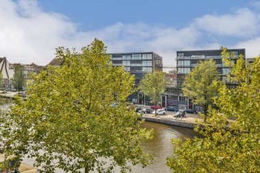 Canlı bir şehir manzarası, yemyeşil ve yansıtıcı sularla çevrili sakin bir su yolu boyunca çağdaş binalar sergiliyor. Şehir ve doğa aşıkları için mükemmel..