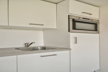 Beyaz dolaplar, paslanmaz çelik aletler ve temiz bir tezgahın olduğu gösterişli ve çağdaş bir mutfak. Modern yaşam alanları için ideal.