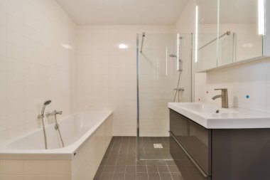 Bu çağdaş banyo cam duşlu, zarif aksesuarlı ve temiz çizgiler ve nötr renklerle tamamlanmış geniş bir küvet içerir..