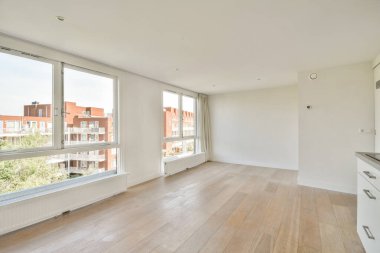 Geniş pencereli, minimalist bir tasarım ve çağdaş bir his için ahşap döşeme sergileyen geniş doğal ışığa sahip, havasız, dağınık bir alan..