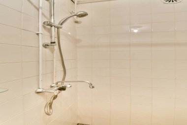 Beyaz fayanslı duvarlar, paslanmaz çelik eşyalar ve modern banyo tasarımı sergilenen cam bir raf içeren temiz ve minimalist bir duş alanı..
