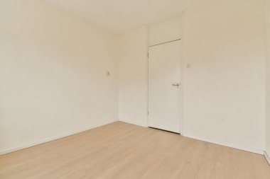 Boş bir odada çıplak duvarlar ve açık ahşap döşemeler var. Uzay boyunca geniş doğal ışık ve sadelikle minimalist bir estetik sergileniyor..