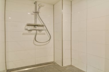 Beyaz fayanslı duvarları ve çağdaş bir duş başlığı olan gösterişli ve minimalist bir duş kabini. Tasarım basitliği ve temizliği vurgular..