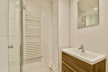 Beyaz fayansların ve sıcak ahşap aksanların yer aldığı, genel estetik cazibeyi ve işlevselliği artıran gösterişli ve çağdaş bir banyo..