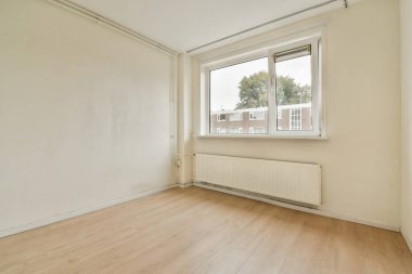 Doğal ışık sunan, tarafsız tonlarla iç mekanın basitliğini gösteren geniş pencereli boş bir oda..