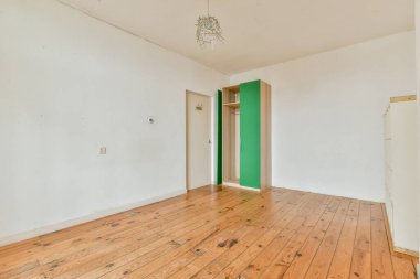 Ahşap döşeme ve basit dekorlardan oluşan parlak, minimalist bir oda. Duvarlar çoğunlukla beyazdır ve gardırop bölgesinde biraz yeşillik vardır, sakin ve ferah bir his verir..