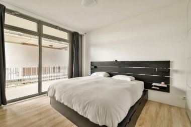 Tarafsız tonlara, rahat bir yatağa ve doğal ışığı davet eden geniş pencerelere sahip zarif ve şık modern bir yatak odası, huzurlu bir atmosfer yaratıyor..