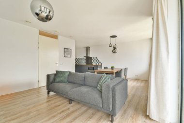 Yeşil yastıklı, gri çizgili bir kanepe arka planda parlak bir mutfak ve modern aydınlatma armatürlerinin yer aldığı şık oturma odası çağdaş bir ortam yaratıyor..