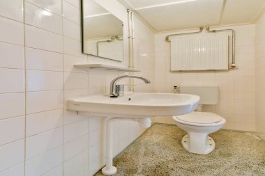 Pürüzsüz ve minimalist bir banyo, beyaz fayanslar, kaidesel bir lavabo, ve kompakt bir tuvalet, kişisel bakım için temiz ve işlevsel bir yer sunuyor..