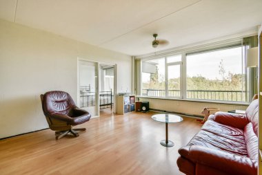 Deri bir kanepe, minimalist bir dekor ve geniş pencerelerden bol miktarda doğal ışık barındıran geniş, modern bir oturma odası..