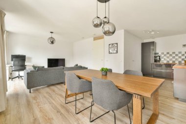 Ahşap bir masa, rahat sandalyeler ve modern dekorun yer aldığı çağdaş bir yemek alanı. Toplantılar ve yemekler için hoş bir atmosfer yaratıyor..