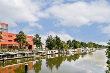 Modern binalar ve canlı bir gökyüzü altında yemyeşil yemyeşil serpilmiş sakin bir nehrin olduğu resim gibi bir manzara. Kentsel doğa entegrasyonunu göstermek için ideal.