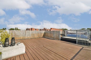 Ahşap döşeme, yeşillik ve berrak mavi gökyüzü altında canlı binaların yer aldığı çağdaş bir çatı katı. Mimari ve doğanın mükemmel bir karışımı..