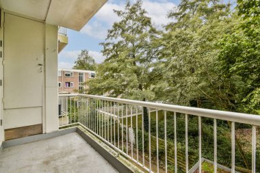 Şık korkuluklu modern bir balkon çevreleyen canlı ağaçlara ve manzaralı alana hayran olmak için avantajlı bir nokta sunuyor, doğanın rahatlığı ve keyfi için mükemmel..