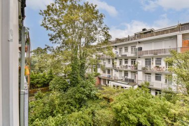 Balkondan manzaralı bir manzara yakınındaki yemyeşil ve ağaçlarla dolu bir apartman kompleksini sergiliyor ve şehirde sakin bir atmosfer yaratıyor..