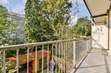 Yeşil ağaçların ve bahçenin korunduğu sakin bir balkon manzarası. Rahatlamak ve güzelliğin tadını çıkarmak için mükemmel..