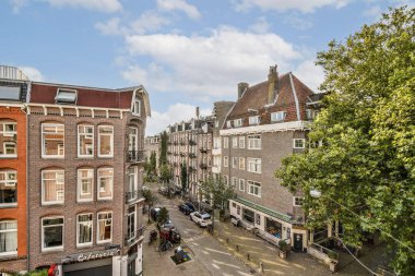 Amsterdam 'da tarihi mimarinin sergilendiği canlı bir cadde manzarası, yemyeşil ve canlı bir atmosfer. Seyahat meraklıları için ideal.