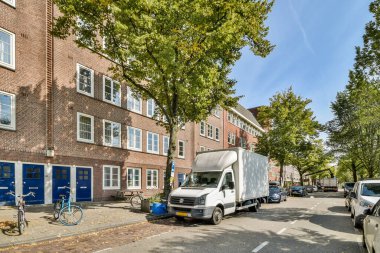 Ağaçlar ve park edilmiş araçlarla dolu modern ve tarihi binaların yer aldığı manzaralı bir cadde, şehir hayatı ve mimarisini gözler önüne seriyor..