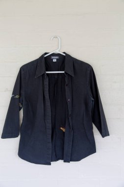 Black button-up shirt with embroidered details on the sleeves, front side visible, hanging on a white wall clipart