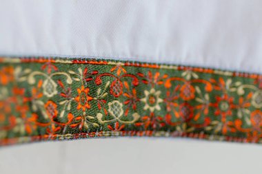 Beyaz pamuklu pantolona işlenmiş, yeşil, turuncu ve krem ipliklerle karışık çiçek ve sarmaşık desenlerini gösteren işlemeli manşet ayrıntıları.