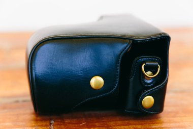 A black leather camera case with brass button details, resting on a rustic wooden surface. The case is closed and shows a sleek, minimalist design, with subtle stitching and a soft texture. clipart