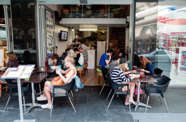 Editorial image of a modern cafe in Sydney, featuring both indoor and outdoor seating. Patrons enjoy meals and drinks in a vibrant, social atmosphere with colorful decor clipart