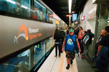 Editorial image of a Sydney Trains platform, showing a mix of commuters, station staff, and a train displaying the 