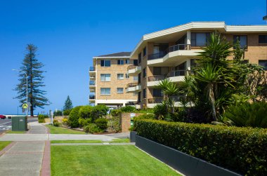 Balkonları ve canlı bahçeleri olan çağdaş deniz manzaralı bir sahil yolu boyunca NSW, Avustralya 'daki berrak mavi gökyüzünün altında yer alan apartmanlar..