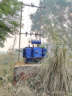 Mavi gökyüzüne karşı yüksek voltajlı trafo. Elektrik akımı yeniden dağıtım istasyonu. Trafo istasyonu ve köydeki elektrik hatları. 18 Aralık 2022 Varanasi Uttar Pradesh Hindistan