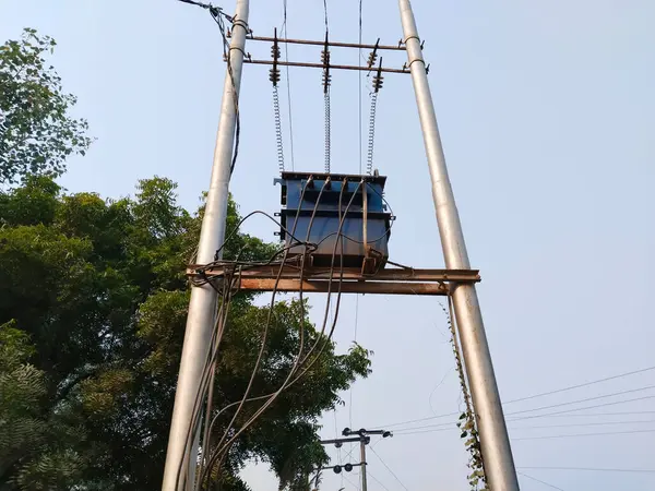High voltage transformer against the blue sky. Electric current redistribution substation. Transformer station and power lines on the street in village. 18 December 2022 Varanasi Uttar Pradesh India