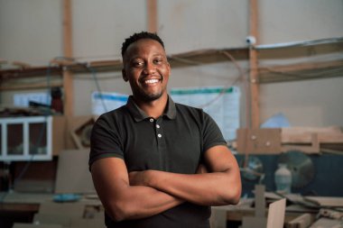 Genç Afrikalı adam fabrikada kollarını kavuşturuyor.