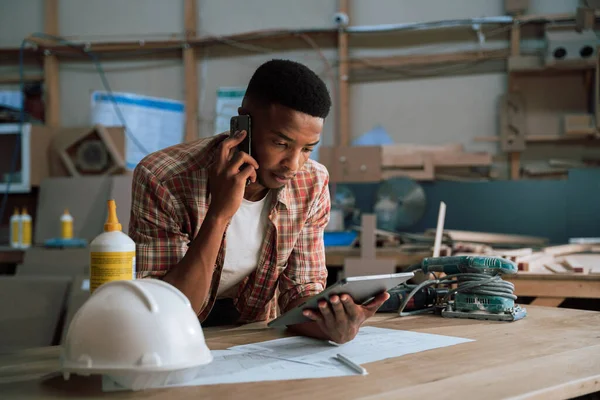 Young African carpenter talking to contractor on cellphone