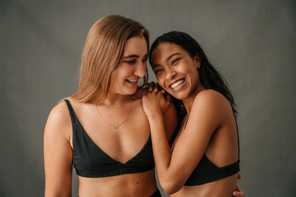 Close up two girlfriends arm in arm standing together smiling in the studio. High quality photo
