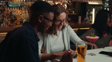 diverse group of friends sitting in restaurant looking at selfies on cellular device laughing. High quality 4k footage
