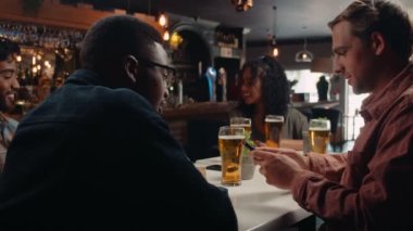 Caucasian male texting on cellular device while out for dinner with friends having beers. High quality 4k footage