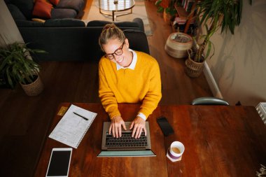 Beyaz kadın evde çalışıyor. Oturma odasında dizüstü bilgisayarla yazı yazıyor. Yüksek kalite fotoğraf