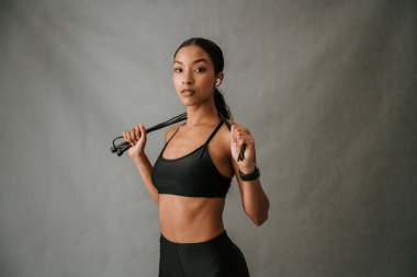 Omuzlarının üzerinden ip atlayan ve spor salonuna başlamaya hazır genç çoklu etnik odaklı dişi kulak kapsülleri. Yüksek kalite fotoğraf