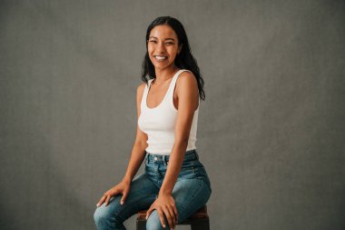 Stüdyoda çok ırklı bir kadın gülümsüyor ve iki dizinin üzerinde oturuyor. Yüksek kalite fotoğraf