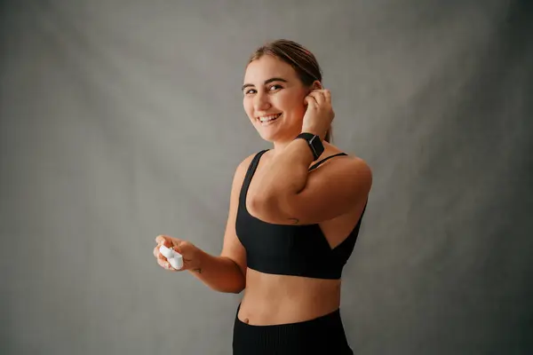 Young smiling Caucasian woman putting her ear pods in and wearing her smart watch in the studio . High quality photo