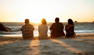 Sahilde oturmuş okyanusu izleyen dört genç arkadaş. Yüksek kalite fotoğraf
