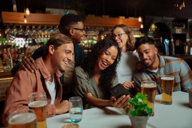 Çok kültürlü bir arkadaş grubu hücresel cihazla yemek yerken selfie çekiyor. Yüksek kalite fotoğraf